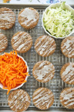Sourdough discard zucchini carrot muffins with apple cider glaze drizzled on top, cooling on a wire rack with bowls of shredded zucchini and fresh grated carrot alongside.
