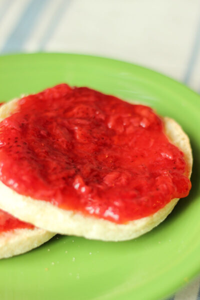 A green plate holds an English muffin covered in beautiful strawberry freezer jam.