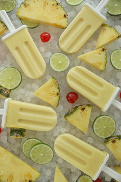 Piña colada popsicles on crushed ice with fresh lime slices, pineapple wedges, and maraschino cherries.