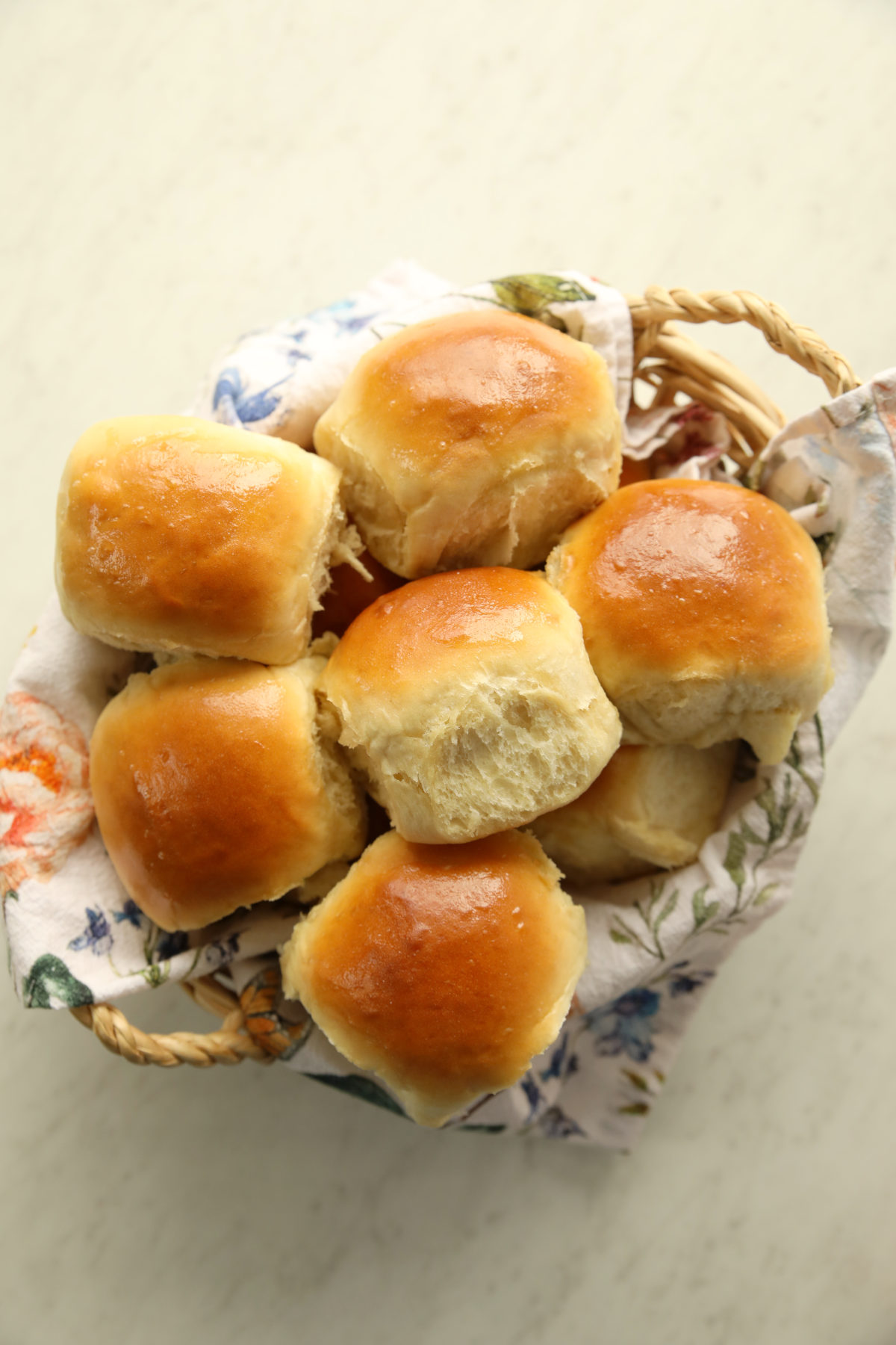 Golden, butter-rubbed sourdough discard dinner rolls piled in a floral-lined basket.