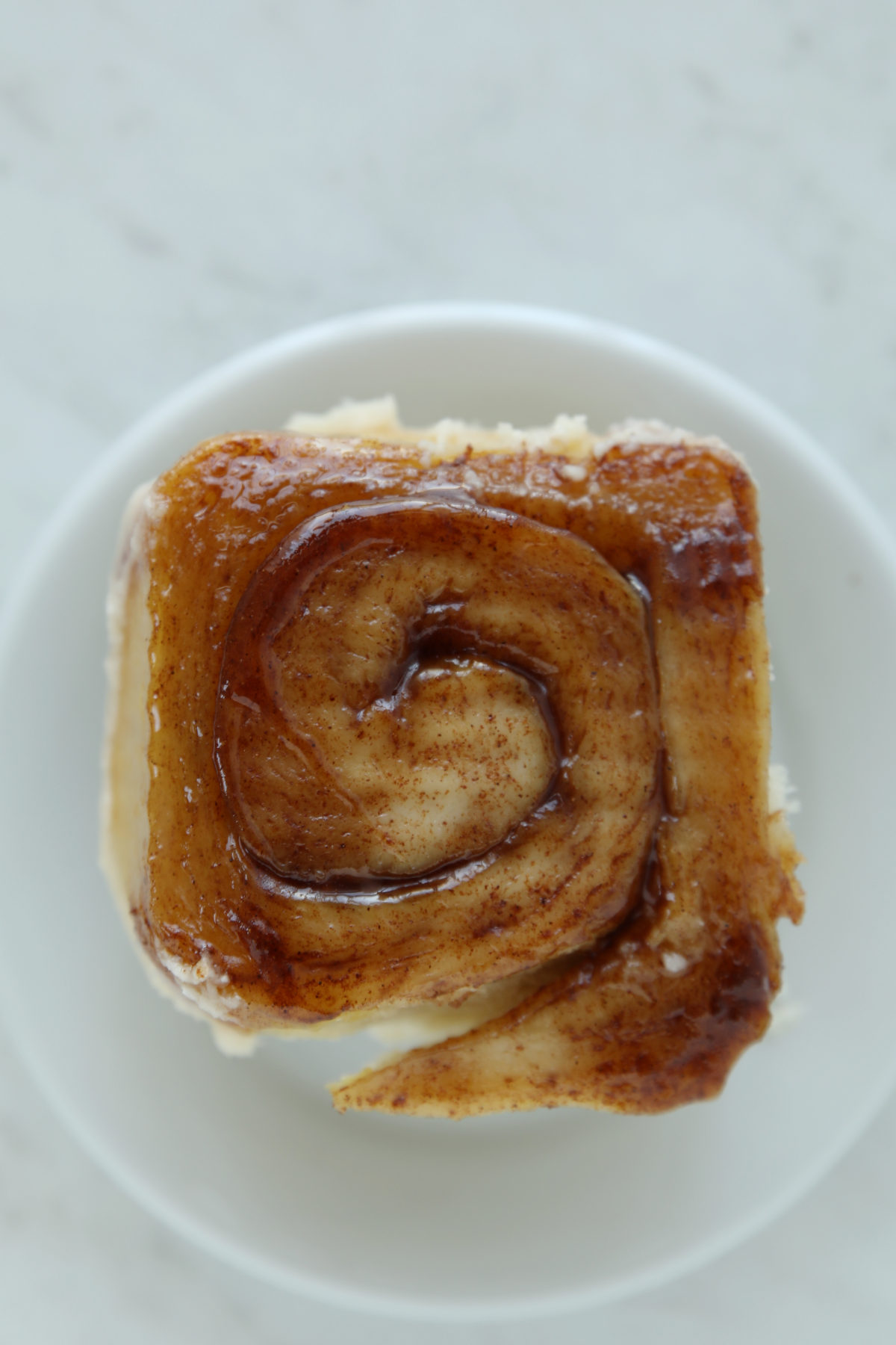 A single sourdough cinnamon roll flipped upside down on a white plate, showing the sticky caramelized brown sugar bottom.