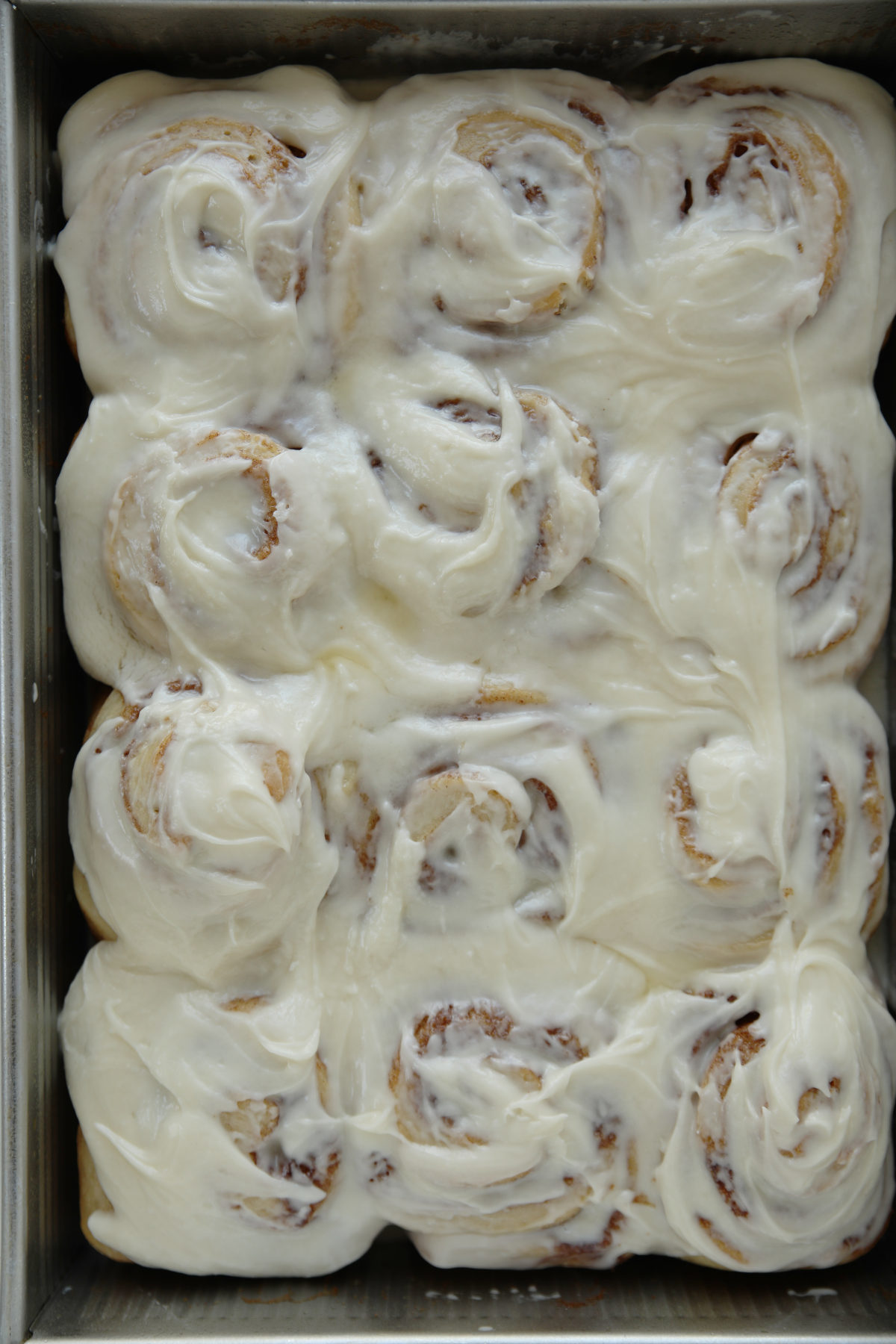 A full pan of sourdough cinnamon rolls generously covered in swirled buttercream glaze, showing 12 rolls in a metal baking pan.