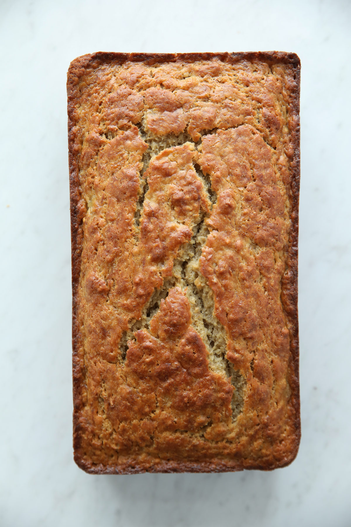Whole loaf of sourdough discard banana bread on white marble, golden cracked crust top-down