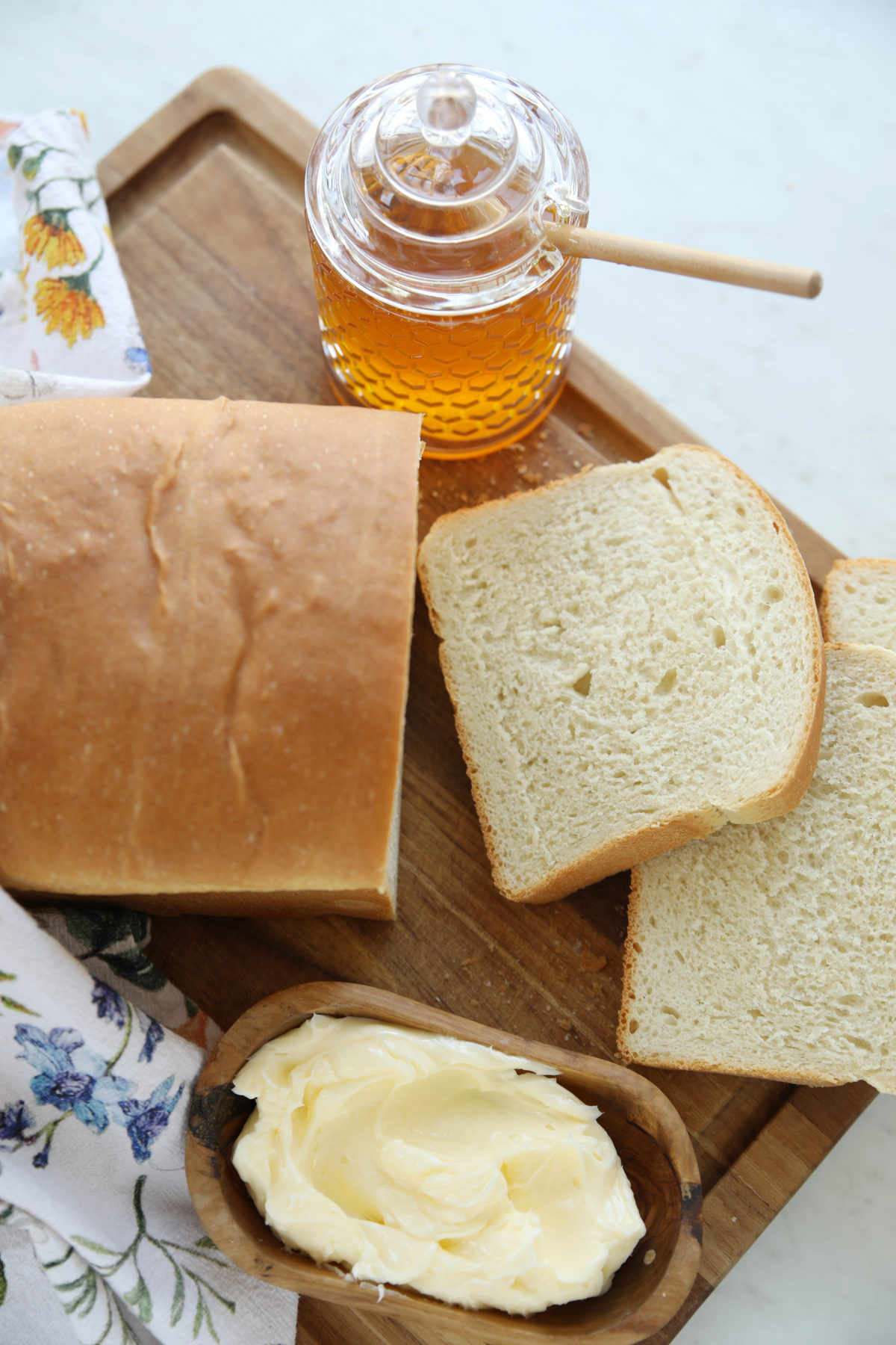 Overhead view of a sourdough discard sandwich bread loaf with slices fanned out on a wood cutting board with a bowl of softened butter and jar of honey