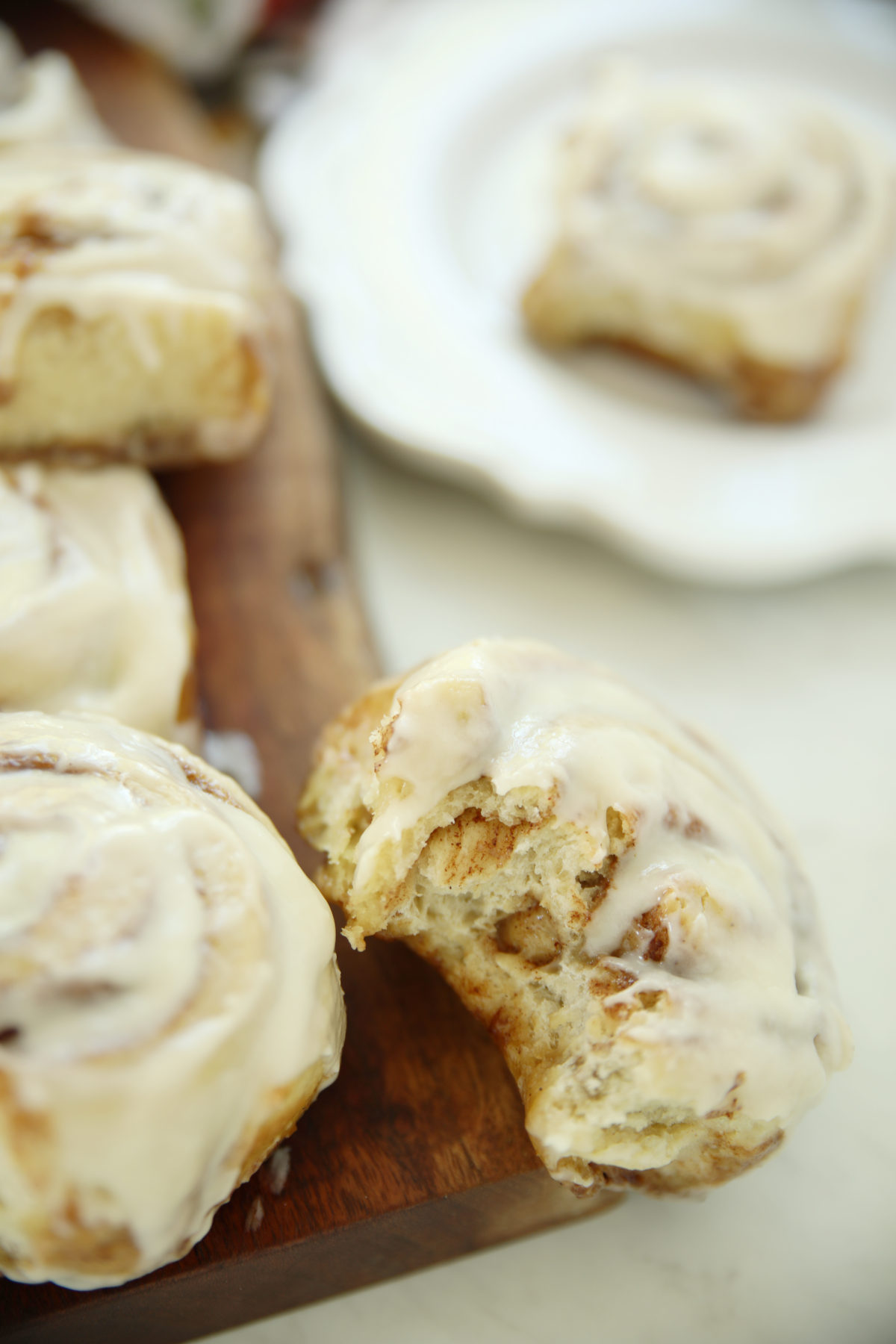 Soft sourdough discard cinnamon roll broken open on a wooden board showing fluffy layers with buttercream glaze