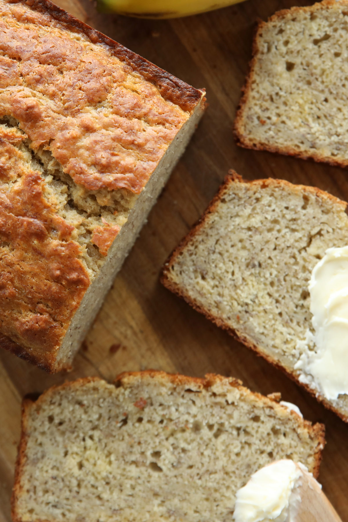 Sliced sourdough discard banana bread on a wooden board, golden crust with one slice spread with butter