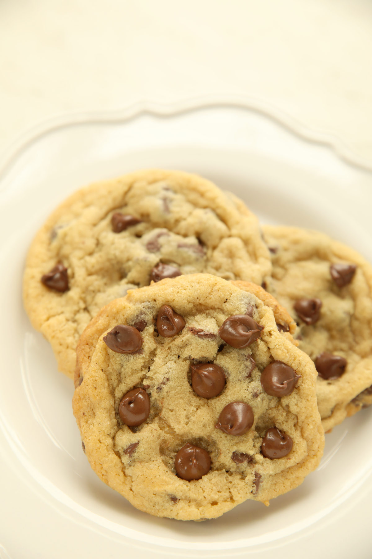 Three chewy sourdough discard chocolate chip cookies with glossy melted chocolate chips stacked on a white plate.