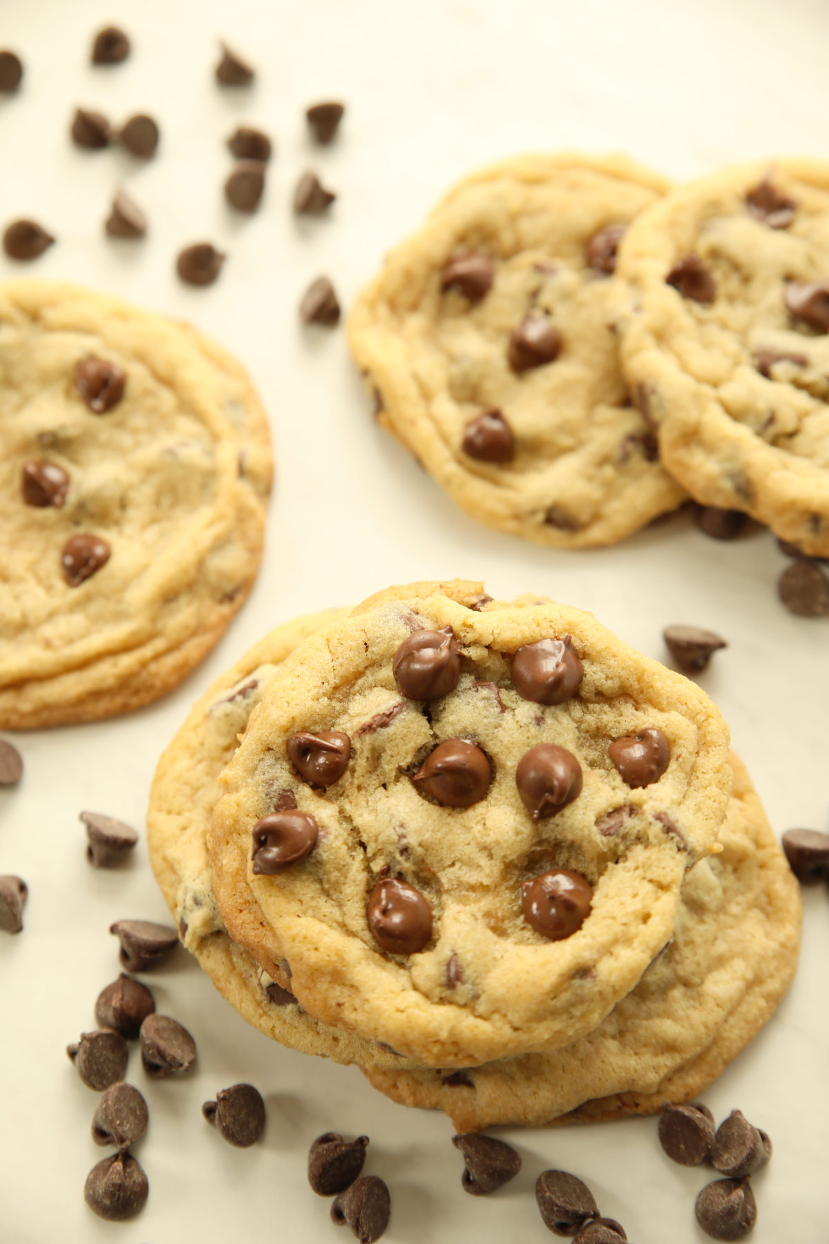 Thick and chewy sourdough discard chocolate chip cookies stacked on a white surface with chocolate chips scattered around them.