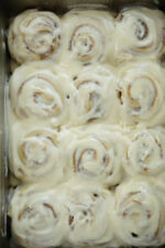 Twelve sourdough discard cinnamon rolls in a metal pan covered in thick swirled buttercream glaze