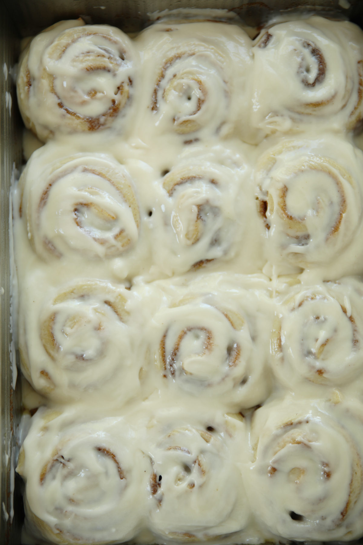Twelve sourdough discard cinnamon rolls in a metal pan covered in thick swirled buttercream glaze