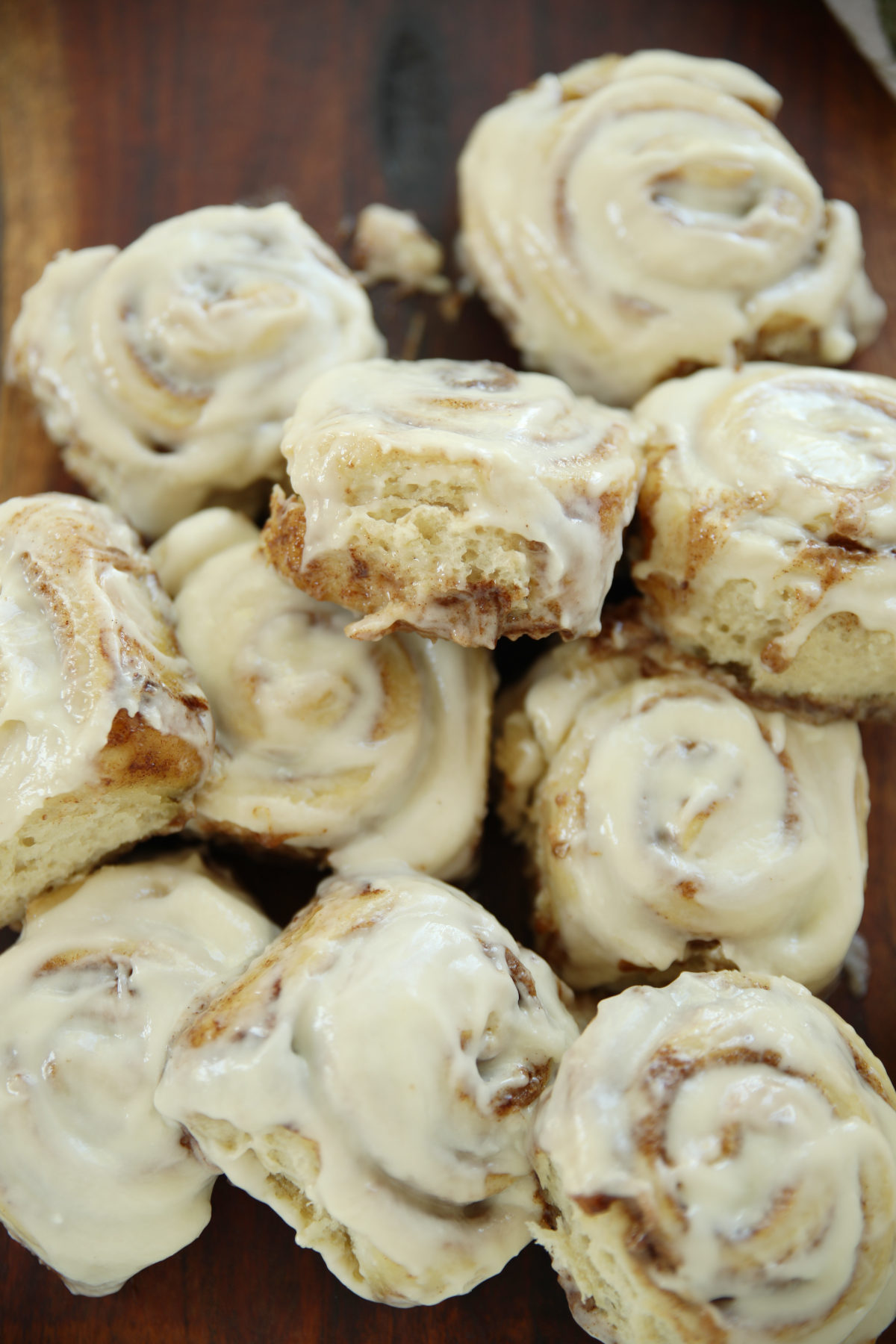 Sourdough discard cinnamon rolls piled on a wooden board with buttercream glaze and one roll showing the soft fluffy interior