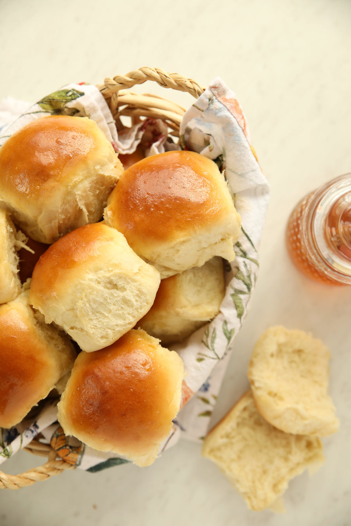 Golden, butter-rubbed sourdough discard rolls piled in a floral-lined basket with a jar of honey and a torn roll showing the soft, fluffy interior.
