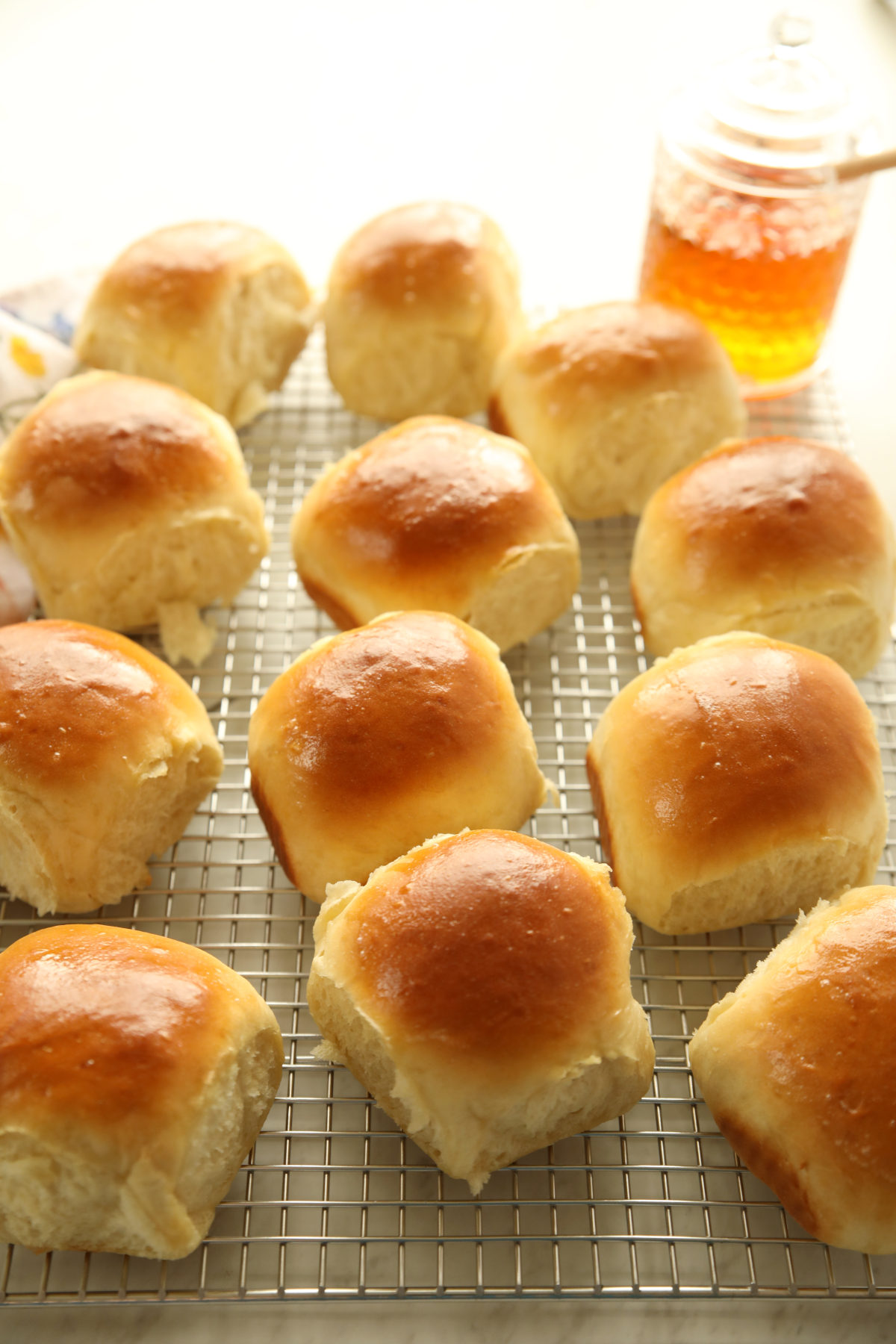 Golden sourdough discard dinner rolls cooling on a wire rack with a jar of honey in the background.