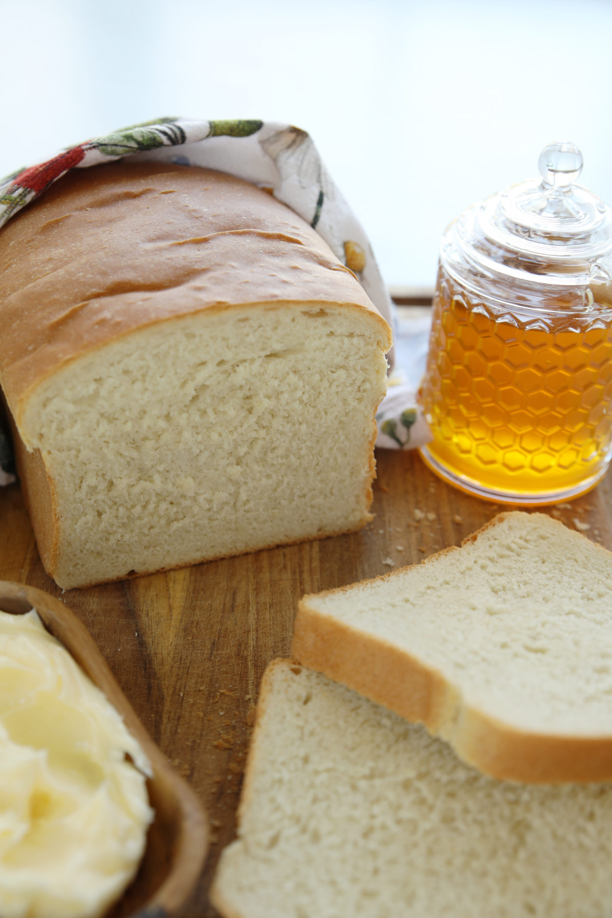 Sliced sourdough discard sandwich bread showing the soft tender crumb on a wood cutting board with a bowl of butter and honey