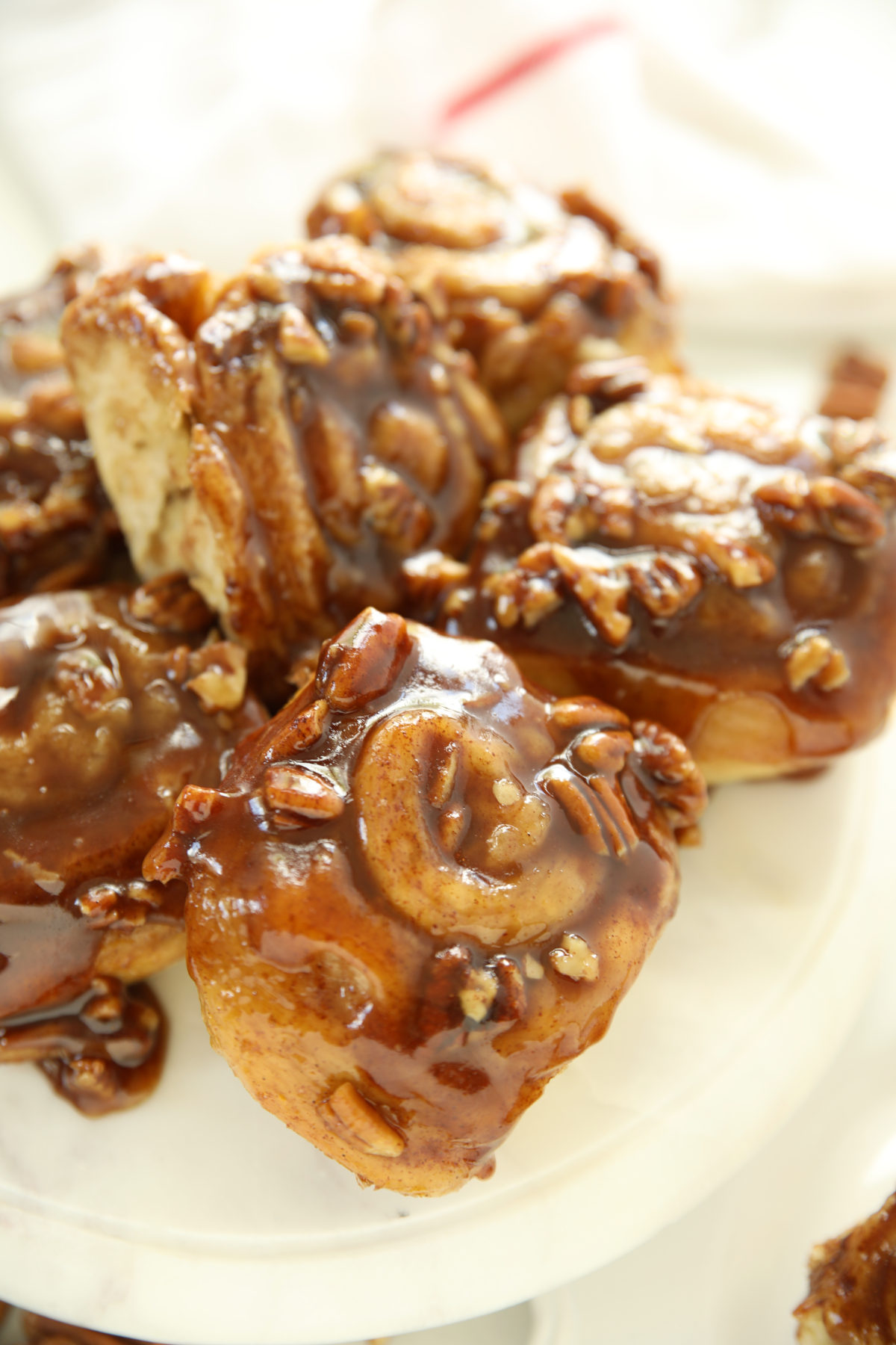 Close up of sourdough discard pecan sticky buns on a white cake stand with gooey caramel syrup dripping down the sides