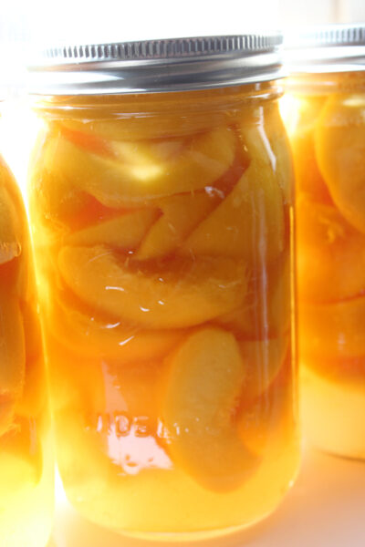 Glass jars of sliced canned peaches in syrup, ready for water bath canning