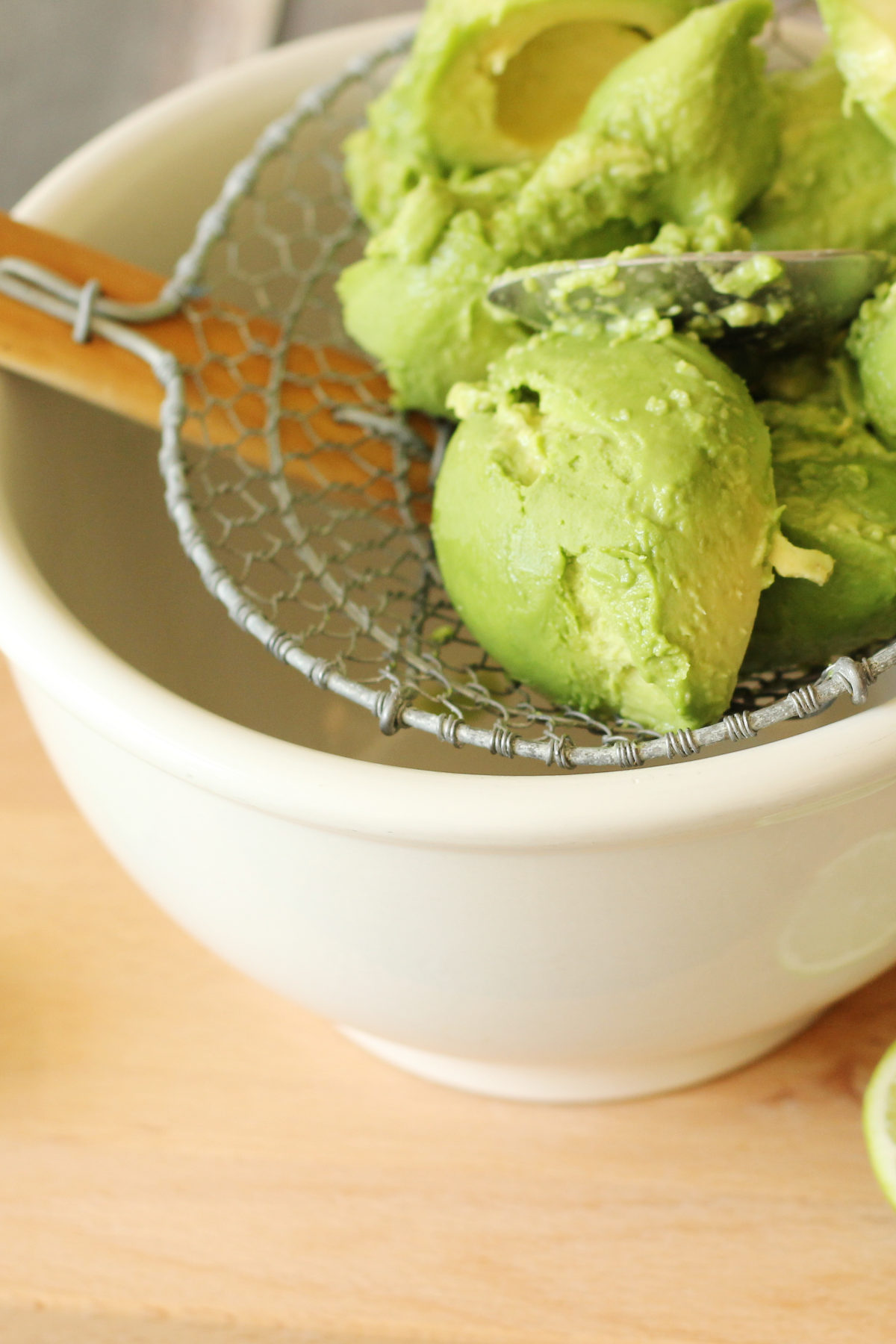 Halved avocados being pressed through a wire skimmer spoon into a bowl for chunky guacamole texture