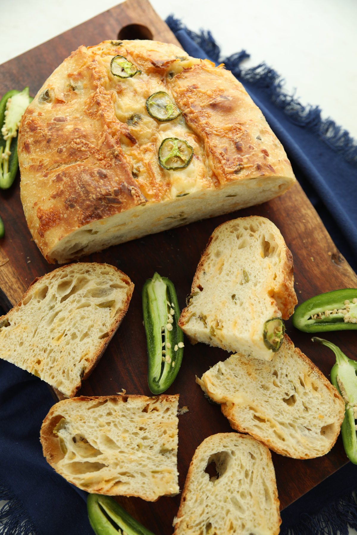 Sliced jalapeño cheddar sourdough bread on a wood cutting board, showing the melty cheese-topped crust and cheese-and-jalapeño-flecked crumb
