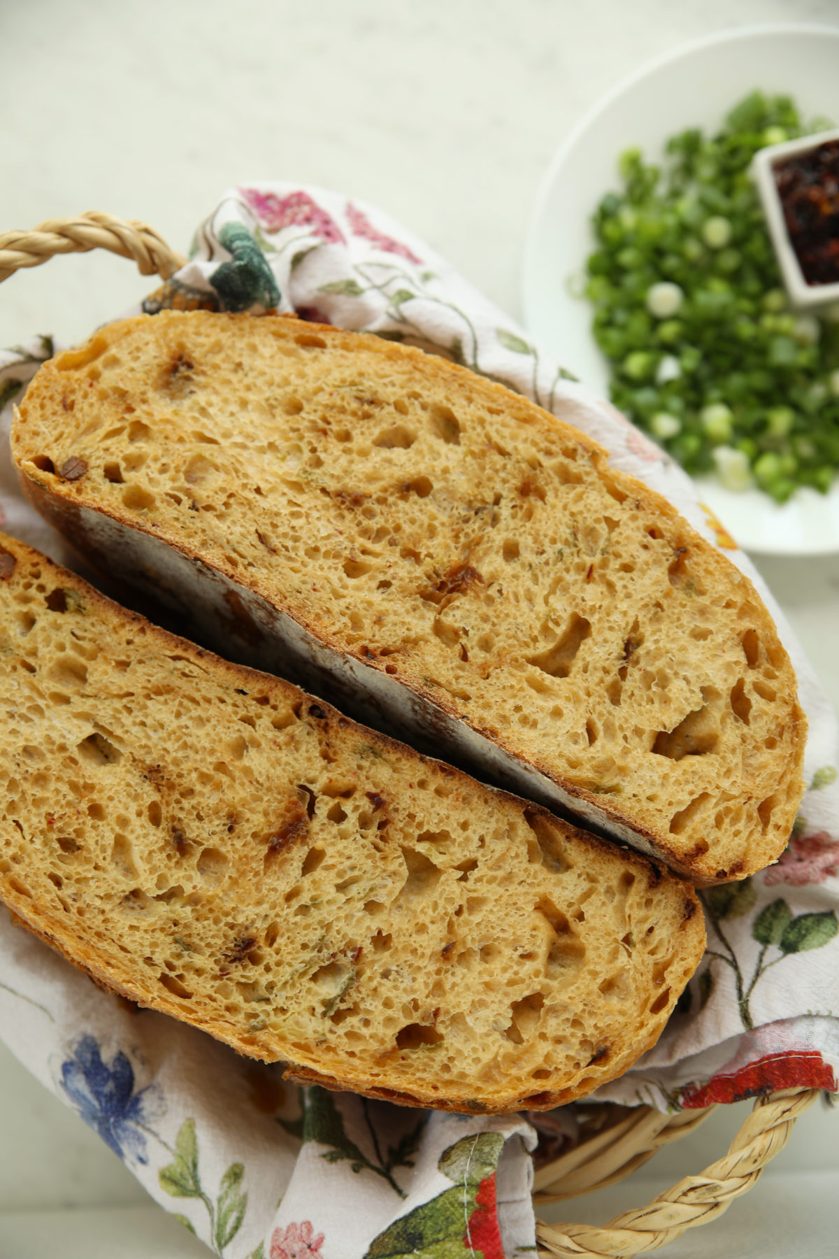 Sliced loaf of chili crisp green onion sourdough bread showing the crumb, with green onions and chili crisp in the background.