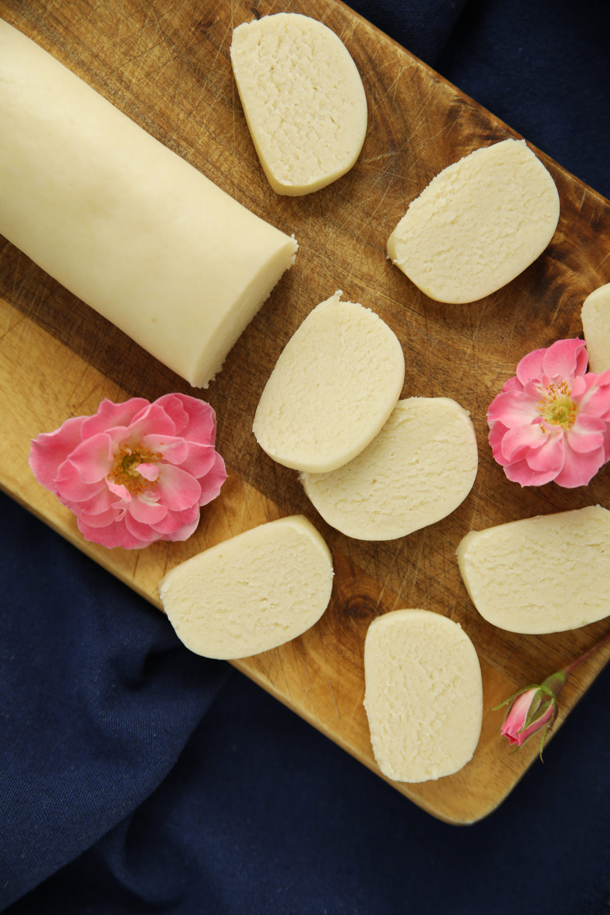 Sliced homemade marzipan log on a wood cutting board, garnished with pink roses