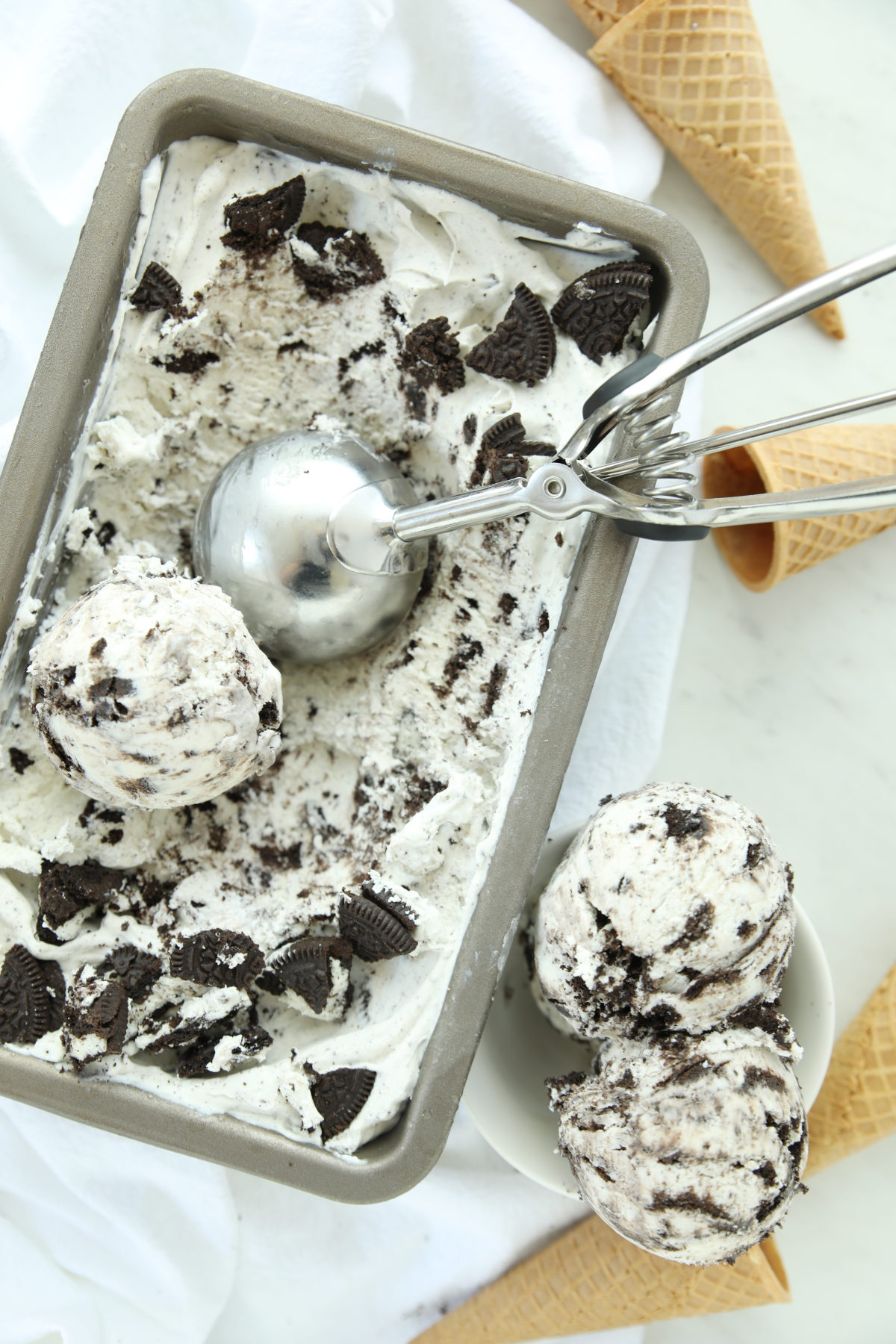 A metal ice cream scoop lifting a scoop of cookies and cream ice cream from a loaf pan