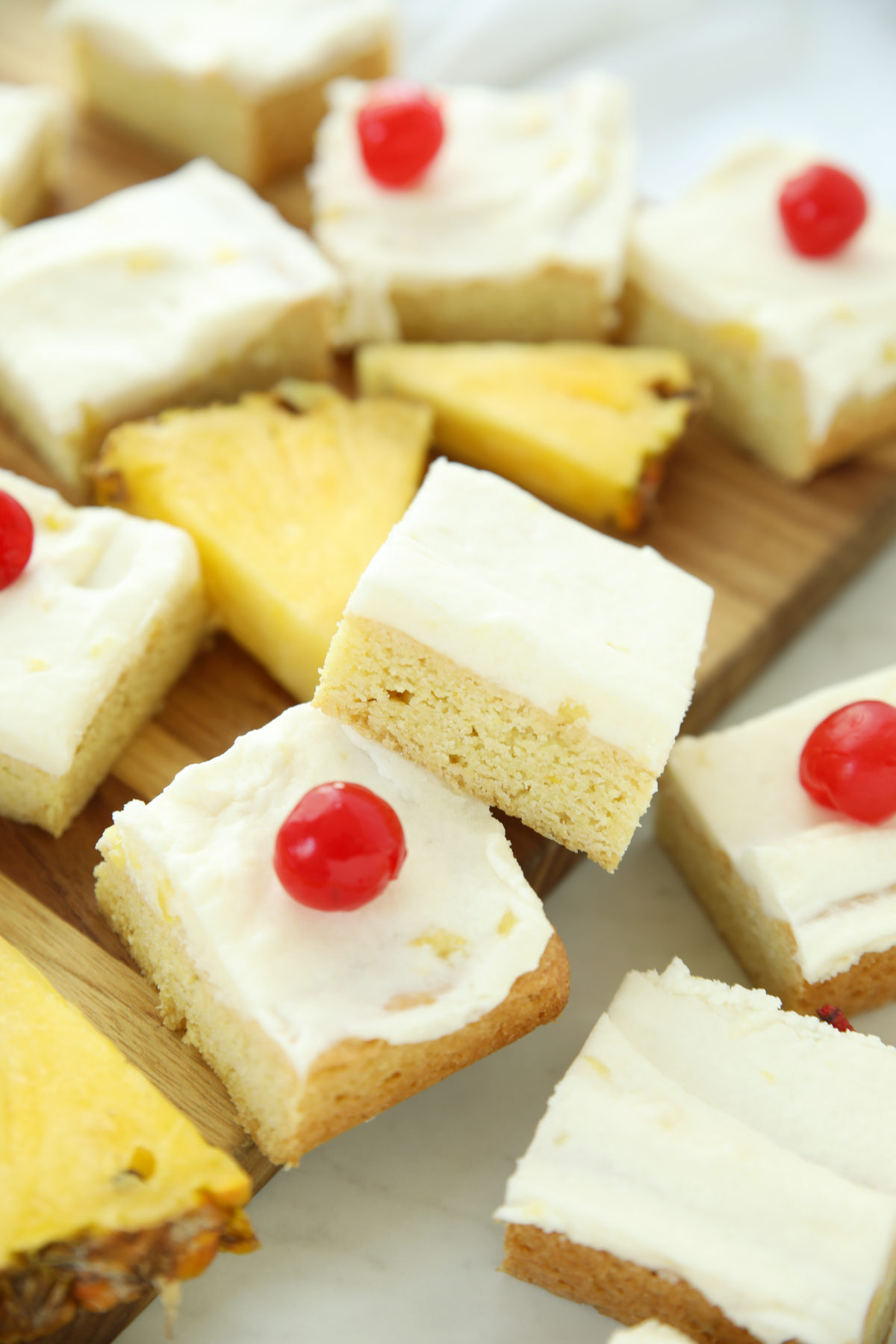 Close-up of a pina colada cookie bar cut in half, showing the soft cookie crumb and coconut-pineapple buttercream layer, topped with a maraschino cherry.