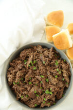 Bowl of melt-in-your-mouth pulled beef garnished with green onions, served with slider buns