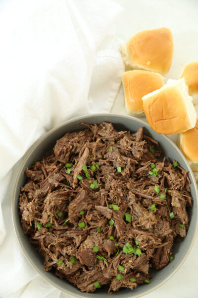 Bowl of melt-in-your-mouth pulled beef garnished with green onions, served with slider buns