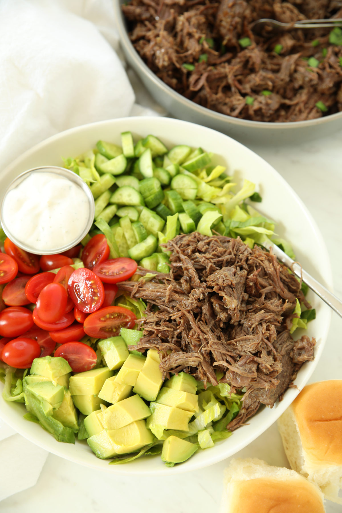 Salad topped with pulled beef, tomatoes, cucumber, avocado, and ranch dressing