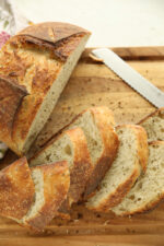Sliced caraway sourdough bread loaf on a wood cutting board, showing the golden crust and crumb flecked with caraway seeds and thyme.