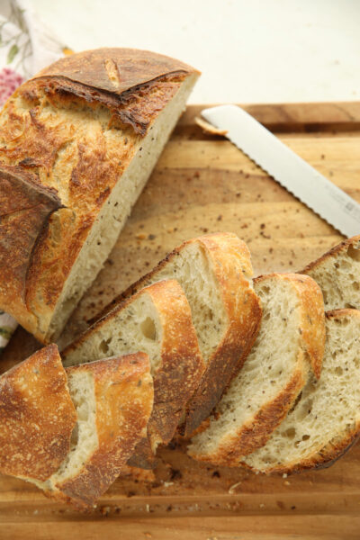 Sliced caraway sourdough bread loaf on a wood cutting board, showing the golden crust and crumb flecked with caraway seeds and thyme.
