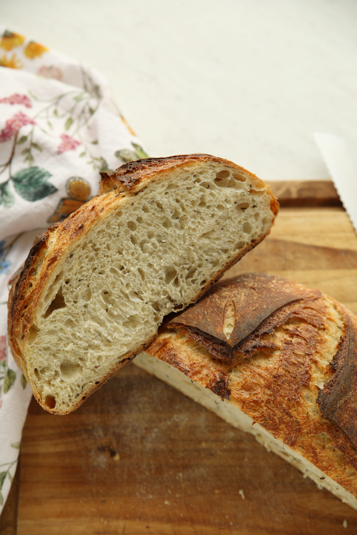 Caraway sourdough bread loaf sliced in half, showing an open crumb speckled with caraway seeds and thyme.