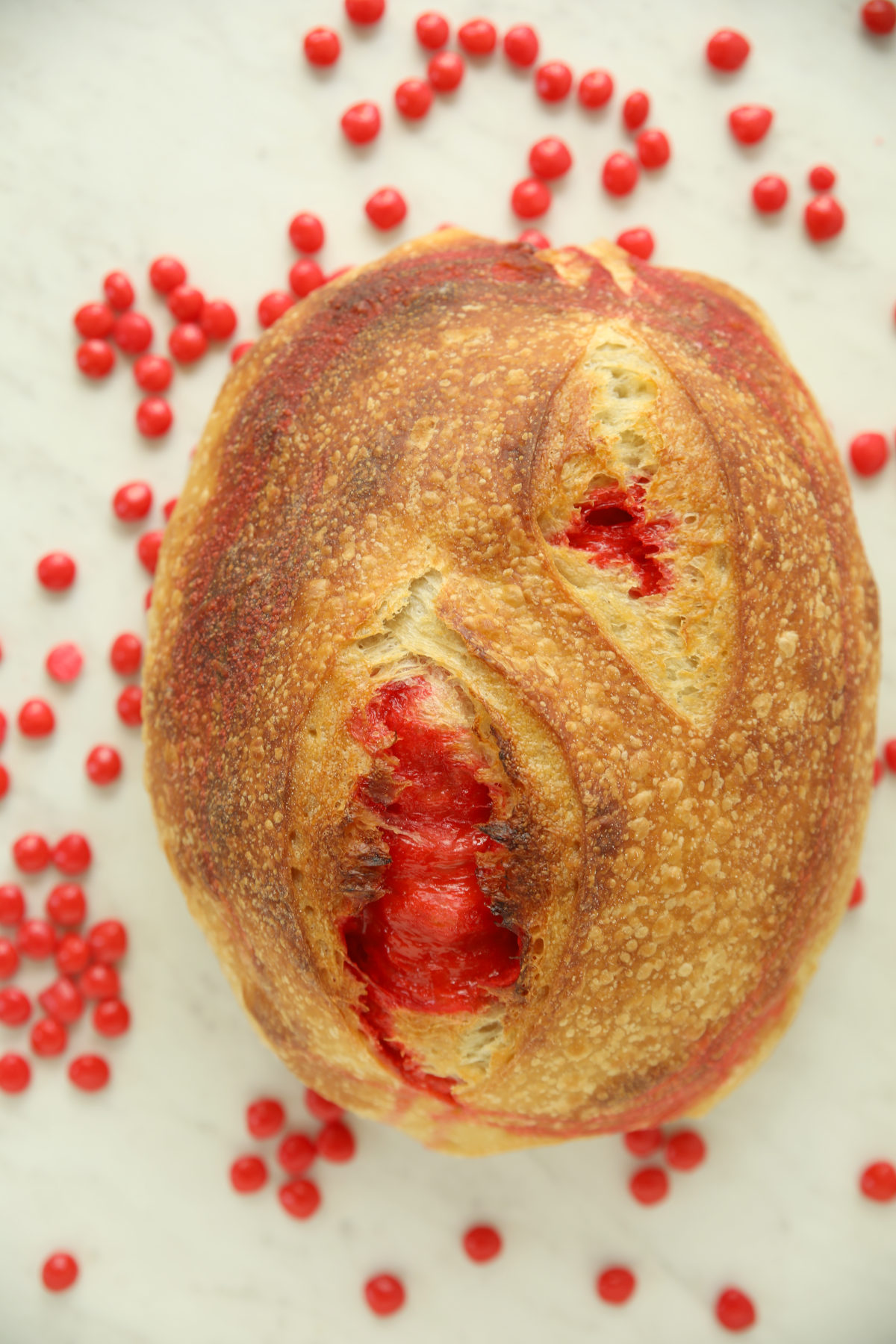 hole Red Hot Cinnamon Sourdough loaf with a single score down the center, red candy visible through the cut, surrounded by scattered red hot candies.