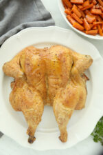 A butterfly chicken on a round white plate next to a dish of candied carrots.
