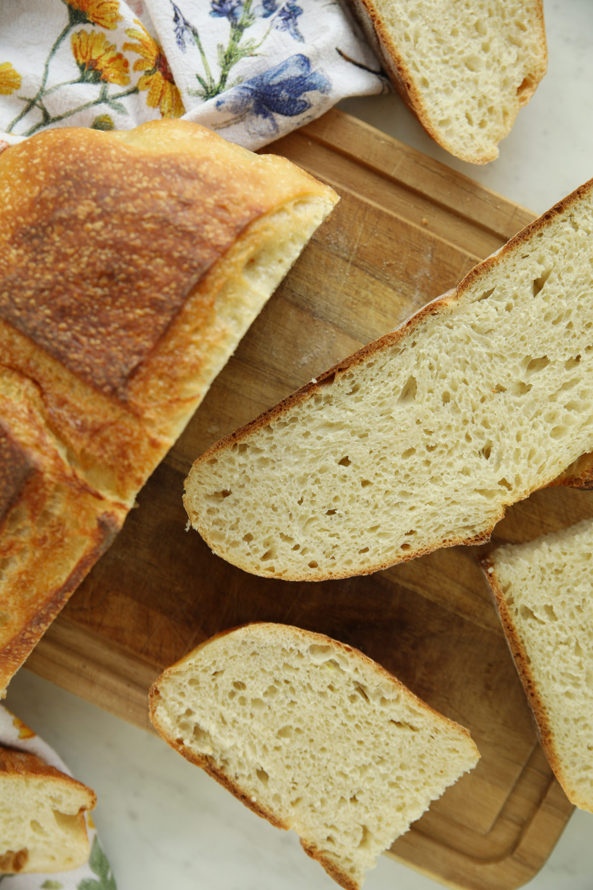 Overhead view of sliced high protein sourdough bread on a wooden board, showing an open, airy crumb across several slices.