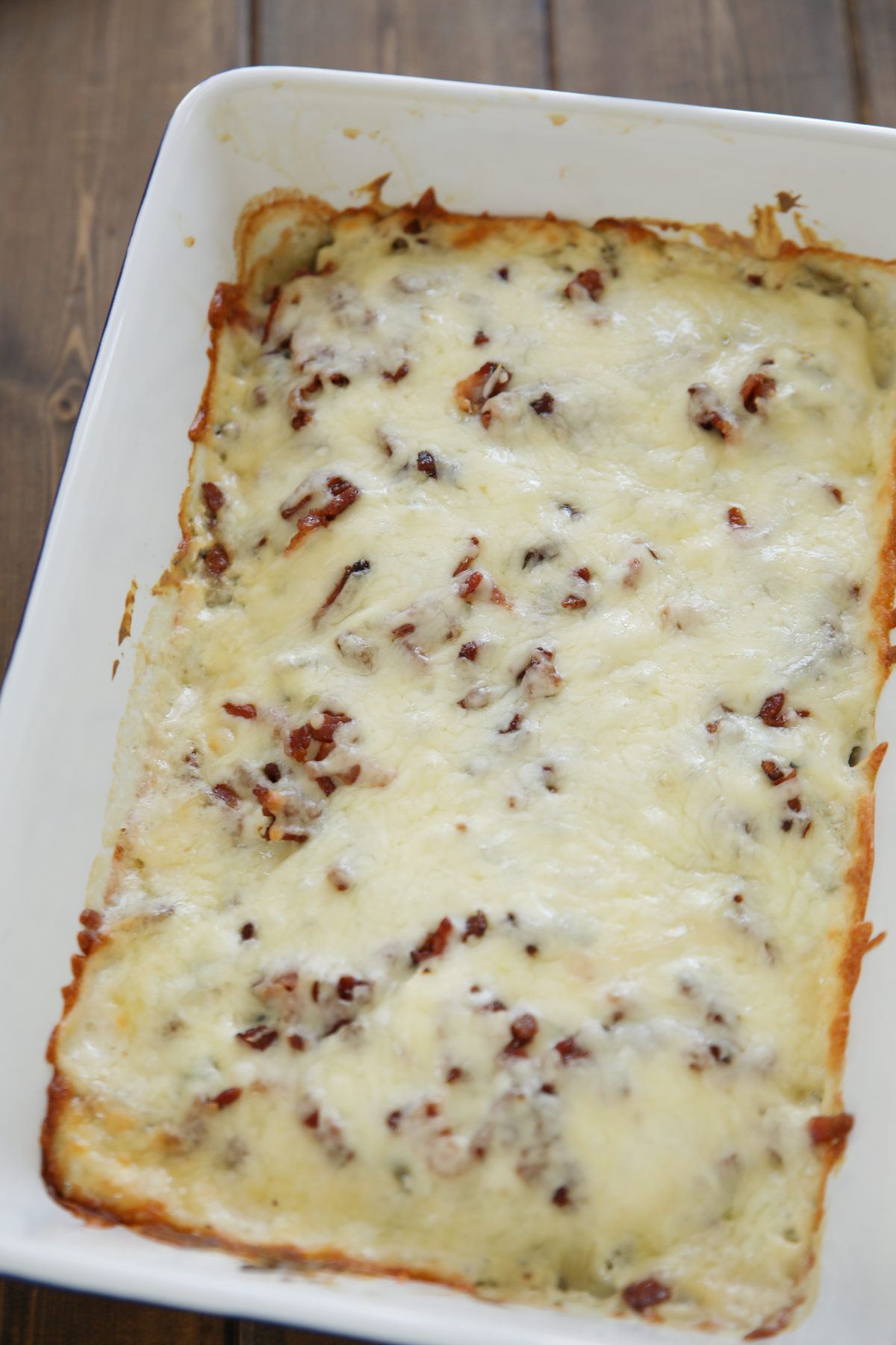 Overhead view of a baked keto chicken casserole in a white dish, topped with melted white cheese and crispy bacon bits, straight out of the oven.