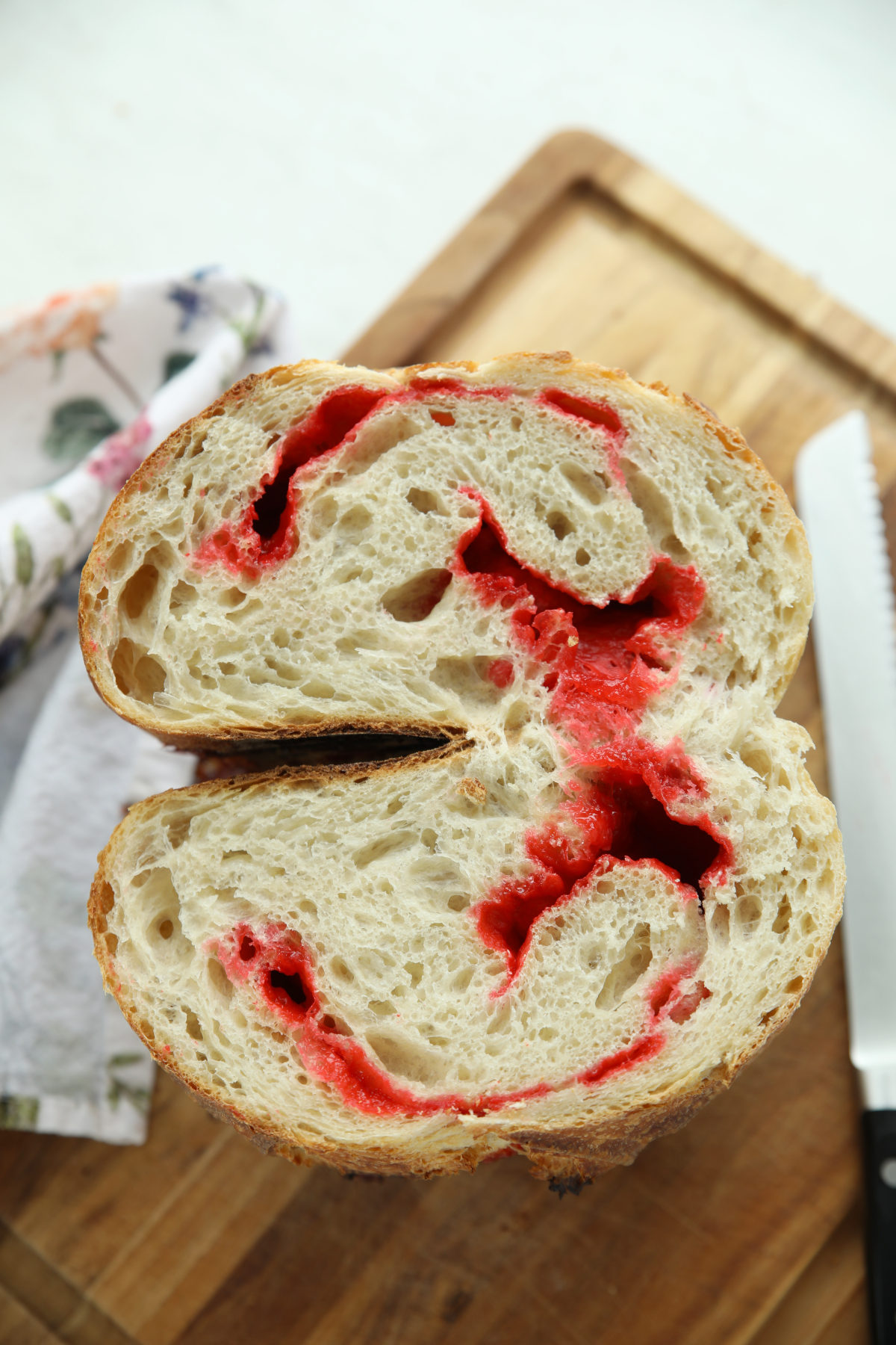 Sliced Red Hot Cinnamon Sourdough Bread showing swirls of melted red candy through the open crumb, on a wooden board with a bread knife.
