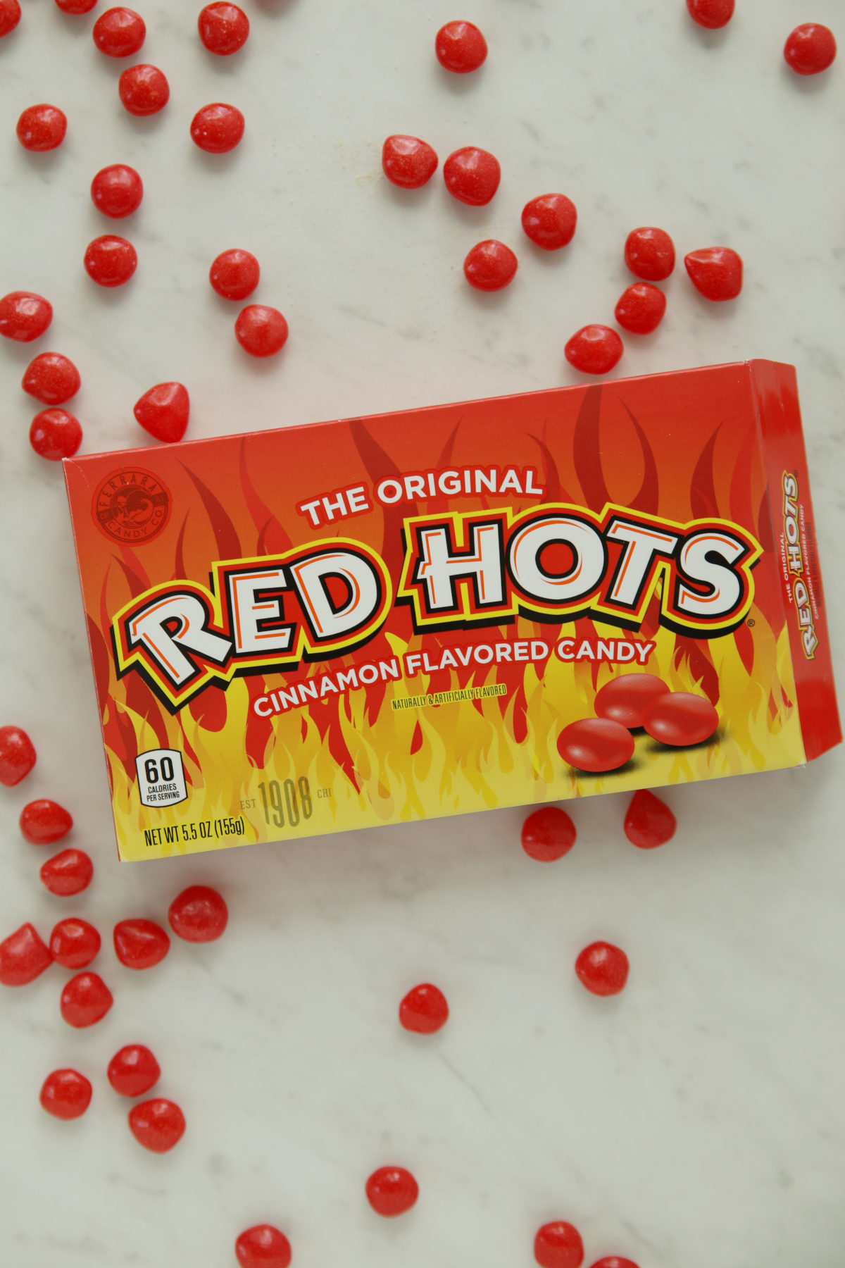Box of Red Hots cinnamon candies scattered on a marble counter, the candies used in this Red Hot Cinnamon Sourdough Bread recipe