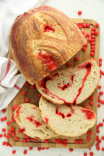 Alt text: "Sliced Red Hot Cinnamon Sourdough Bread showing red candy swirled through the crumb, on a wood board surrounded by scattered red hot candies.