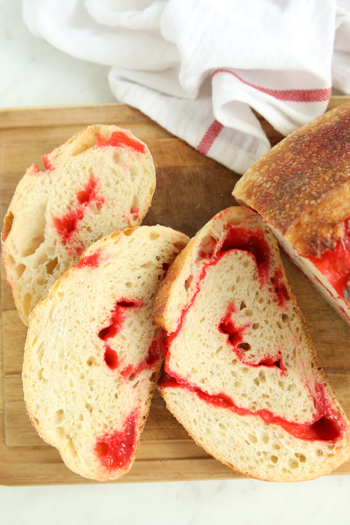 Close-up of sliced Red Hot Cinnamon Sourdough Bread showing the red candy swirl through the crumb, with the whole loaf's cut side visible in the background.